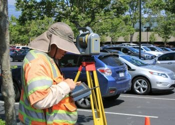 Topógrafo realizando medición geoespacial con estación total en un área urbana.